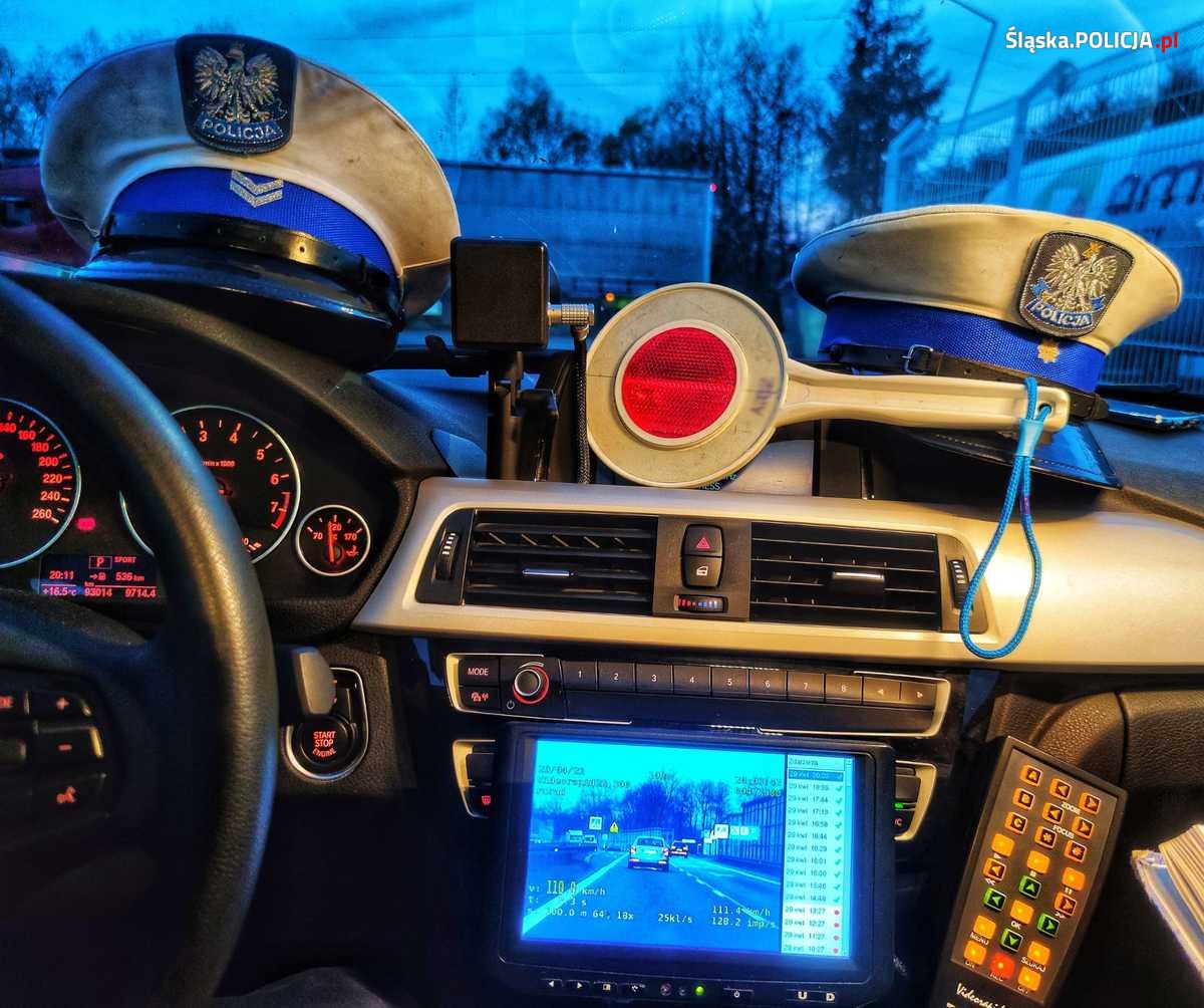 wnętrze policyjnego radiowozu - widać lizak i czapki policyjne i monitoring