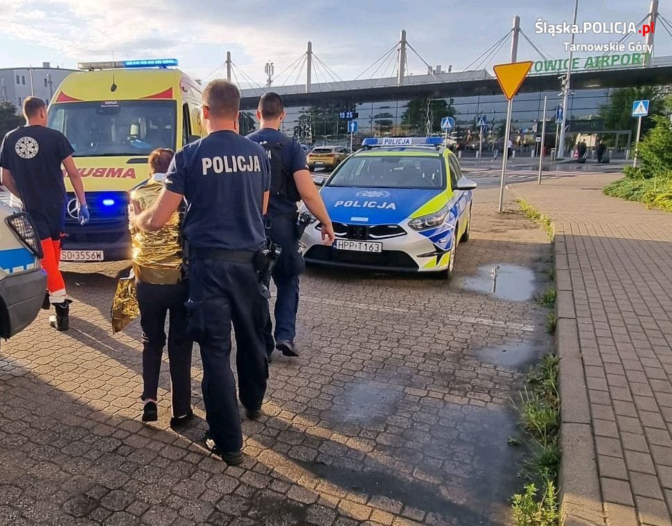 policjanci, radiowóz, karteka i seniorka przed Katowice Airport